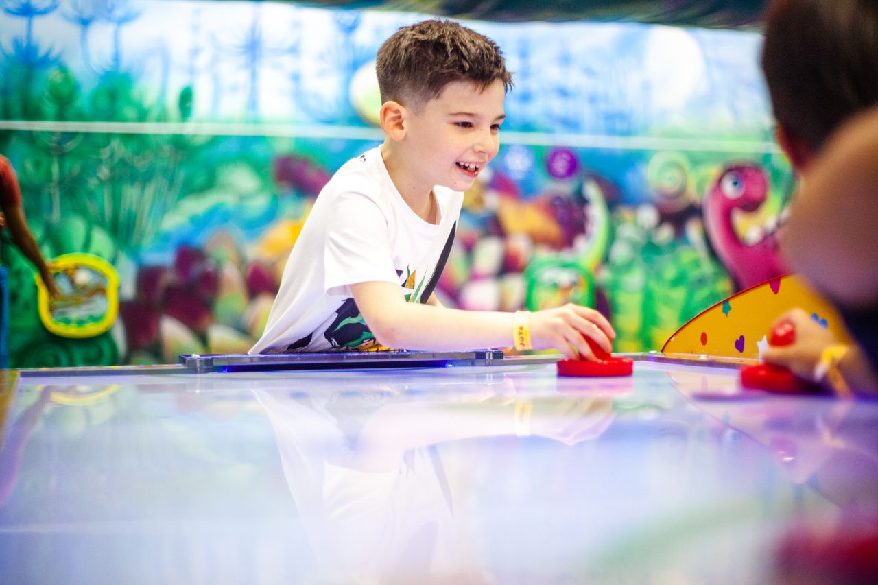 A young boy happily plays air hockey in a vibrant indoor playground in Moscow.