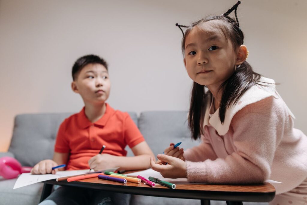 Crafting Captivating Headlines: Your awesome post title goes here Two Asian children drawing with colored pens indoors, showcasing creativity and sibling bonding.